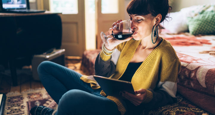 Woman relaxes on couch with ipad and drinks wine